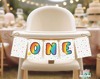 Puede incluir: Una trona blanca con una pancarta que dice "ONE" en colores arcoíris. La pancarta tiene un patrón de estrellas y nubes. La escena sugiere una celebración de primer cumpleaños.