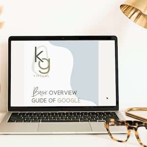 May include: A laptop computer displaying a website with a logo that says "KG Virtual" and the text "Basic Overview Guide of Google". The laptop is on a white desk with a vase of dried flowers, a gold lamp, and a pair of tortoiseshell glasses.