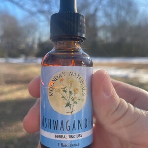 May include: A brown glass bottle with a dropper top and a blue and white label that says "Moonday Naturals Ashwagandha Herbal Tincture 1 fluid ounce".