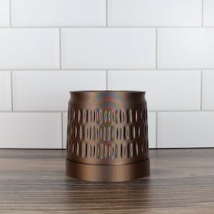 May include: A copper-coloured metal planter with a textured design. The planter is sitting on a wooden surface.
