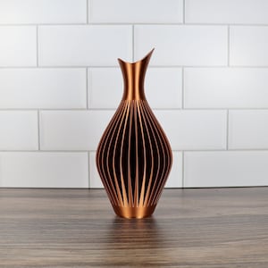 Peut inclure: Un vase de couleur cuivre avec un design géométrique. Le vase est fait d'un matériau qui ressemble au métal et a une finition lisse et brillante.