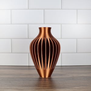 Peut inclure: Un vase décoratif de couleur cuivre avec un design géométrique ajouré. Le vase a une forme ronde et bulbée et un col étroit.
