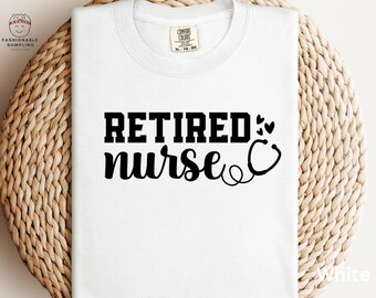 May include: White t-shirt with the words "RETIRED nurse" in black, along with a stethoscope graphic. The shirt has a crew neck and a tag that says "Comfort Colors". The shirt is folded on a woven surface.
