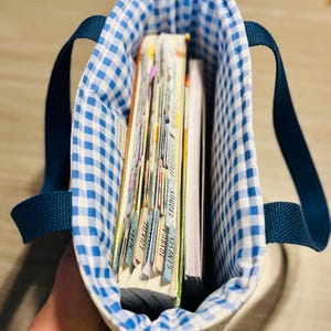 May include: A blue and white gingham tote bag with navy blue handles, filled with books and notebooks. The interior lining of the bag is also blue and white gingham. The books have labeled tabs.
