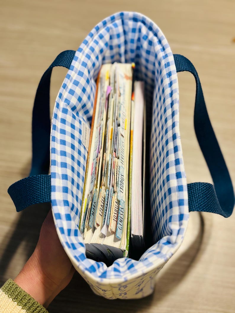 May include: A blue and white gingham tote bag with navy blue handles, filled with books and notebooks. The interior lining of the bag is also blue and white gingham. The books have labeled tabs.