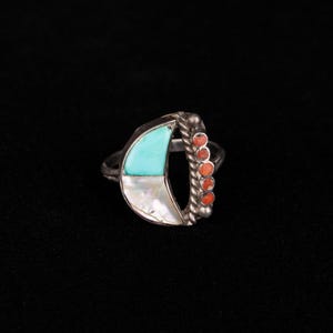 May include: A silver ring with a crescent moon design featuring turquoise and mother-of-pearl inlay. The ring is accented with a row of small red coral stones.
