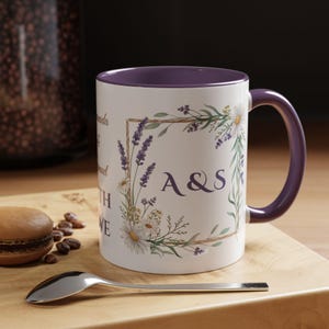 Puede incluir: Taza de cerámica blanca con interior y asa morados. La taza presenta un diseño floral con lavanda y margaritas, y las iniciales "A&S". La taza está sobre una superficie de madera con una cuchara y un macaron.