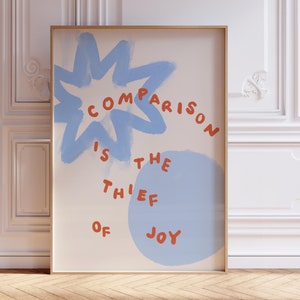 以下が含まれることがあります： 青い白の抽象的なデザインとオレンジ色の「Comparison is the thief of joy」というテキストが書かれた額装されたプリントです。