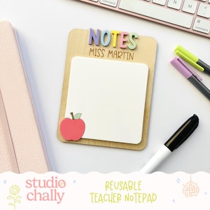 May include: A wooden teacher's notepad with the word "NOTES" in colourful letters and the name "MISS MARTIN". It features a white notepad, a red apple, and the text "REUSABLE TEACHER NOTEPAD". The notepad is surrounded by pens and a keyboard.