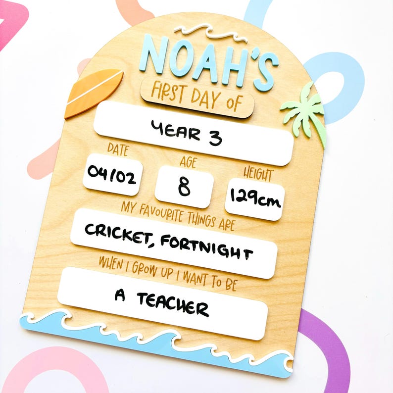 May include: Wooden first day of school sign with the name "Noah's" in blue letters. The sign includes spaces for the date, age, height (129cm), and favorite things, with the text "Cricket, Fortnight" and "A Teacher". A surfboard and palm tree are also featured.