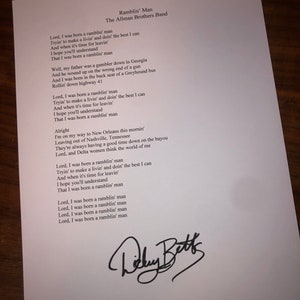 May include: Black and white handwritten lyrics for the song "Ramblin' Man" by The Allman Brothers Band. The lyrics are written in a cursive font and include the signature "Dickey Betts".