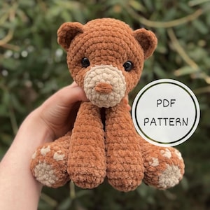 May include: Crochet pattern for a brown teddy bear with beige paws. The pattern is available as a PDF download.