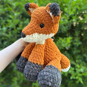 Puede incluir: Un peluche de zorro hecho a mano con ganchillo. El zorro presenta hilo naranja, blanco y gris. El zorro tiene ojos negros y un hocico blanco. Las orejas tienen puntas negras. El peluche es suave y tierno.