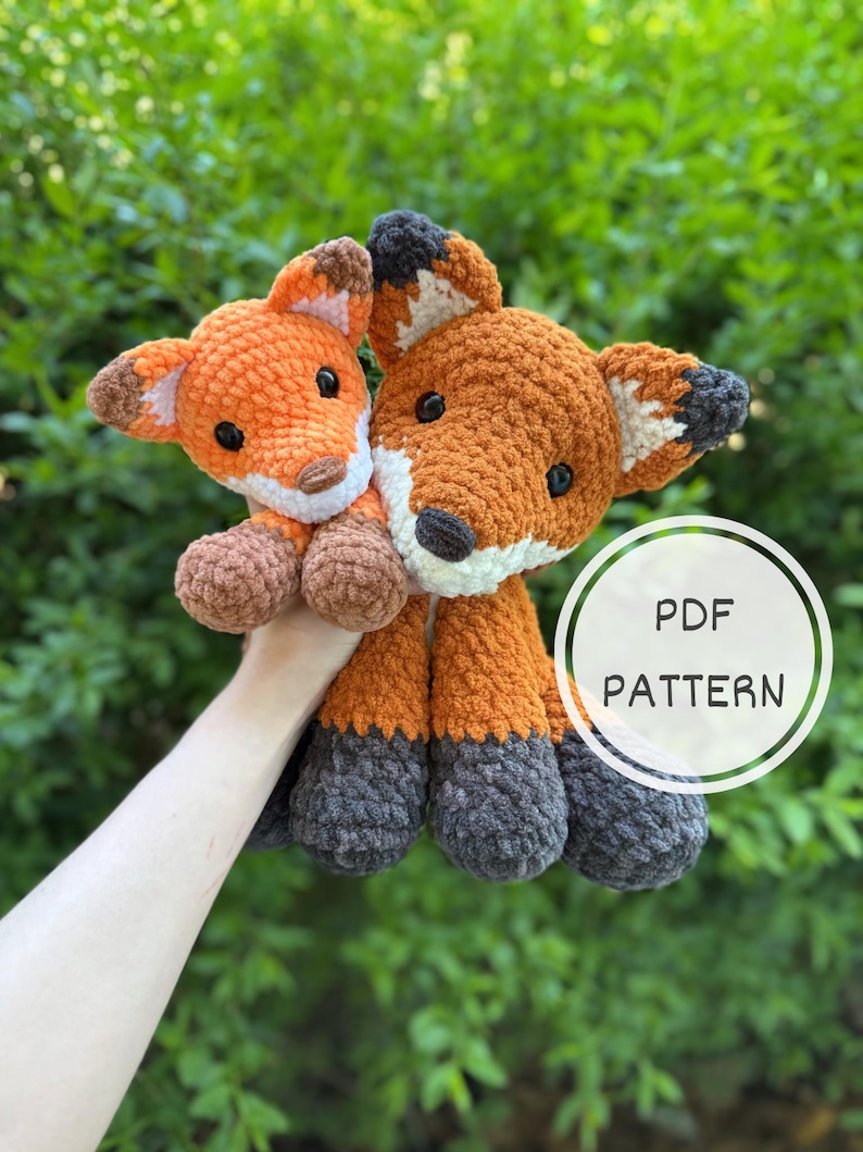 Puede incluir: Dos peluches de zorro de ganchillo. El zorro m&aacute;s grande es naranja, marr&oacute;n, blanco y gris. El zorro m&aacute;s peque&ntilde;o es naranja, marr&oacute;n y blanco. El texto "PDF PATTERN" est&aacute; en un c&iacute;rculo blanco. Los peluches se sostienen sobre un fondo verde.