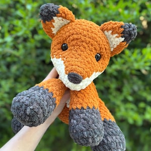 Puede incluir: Un peluche de zorro hecho a mano de ganchillo naranja, blanco y gris. El zorro tiene ojos negros y un hocico blanco. Las orejas y los pies son grises. El zorro es un juguete suave y afelpado.