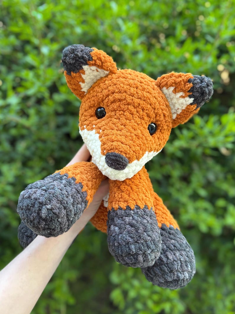 Puede incluir: Un peluche de zorro hecho a mano de ganchillo naranja, blanco y gris. El zorro tiene ojos negros y un hocico blanco. Las orejas y los pies son grises. El zorro es un juguete suave y afelpado.