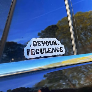 May include: A white sticker with black text that reads "DEVOUR FECULENCE" on a black car window.