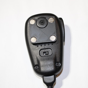 May include: Black handheld radio with a square magnetic mount on the back. The radio has a small switch on the side.