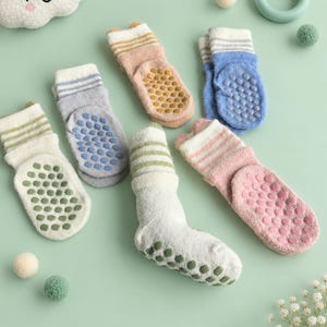 Pode incluir: Uma coleção de seis meias de tornozelo felpudas em várias cores pastel, incluindo creme, azul, rosa e pêssego. Cada meia apresenta listras horizontais no punho e uma sola texturizada com pontos de silicone em relevo para aderência.