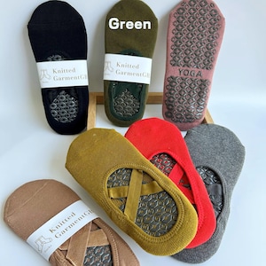 May include: A collection of colorful, no-show socks with non-slip soles. The socks are in various colors, including black, green, red, and gray. Some socks have the text "Knitted Garment GB" on a white label. One pair has the word "YOGA" printed on it.