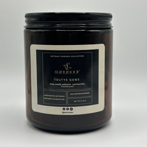 May include: A brown glass jar with a black lid and a white label. The label features the text "sununoor" and "TOUTYS GOWE". The jar contains 156 grams of product and is described as deep, woody, seductive, and luxurious.