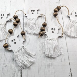 May include: A white ghost garland with brown wooden beads. The ghosts have white fringe and are strung on a twine string.