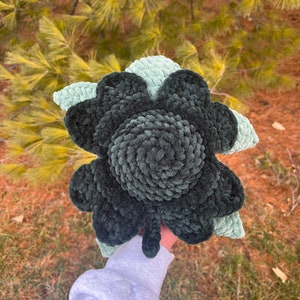 Könnte beinhalten: Eine handgefertigte Plüschblume in Grüntönen. Die Blume hat eine dunkelgrüne Mitte mit helleren grünen Blütenblättern. Das weiche, strukturierte Material verleiht der Blume ein gemütliches Aussehen. Die Blume wird in der Hand einer Person gehalten.