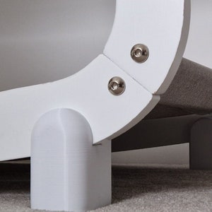 May include: White cat bed with a curved design and a grey fabric lining. The bed has four white plastic feet.