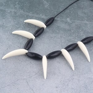 May include: Black and white beaded necklace with a series of pointed white beads alternating with black oval beads.
