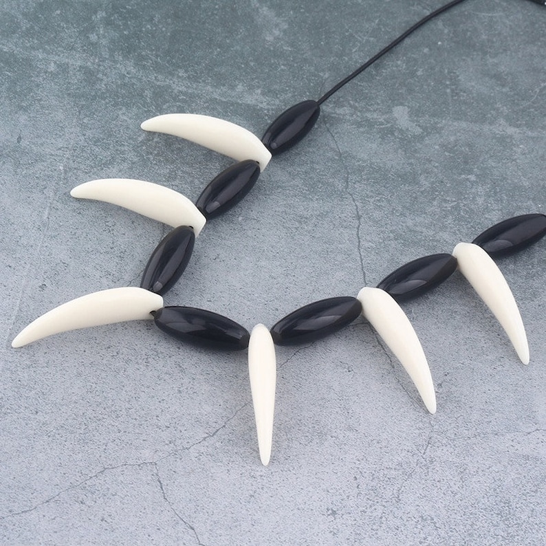 May include: Black and white beaded necklace with a series of pointed white beads alternating with black oval beads.