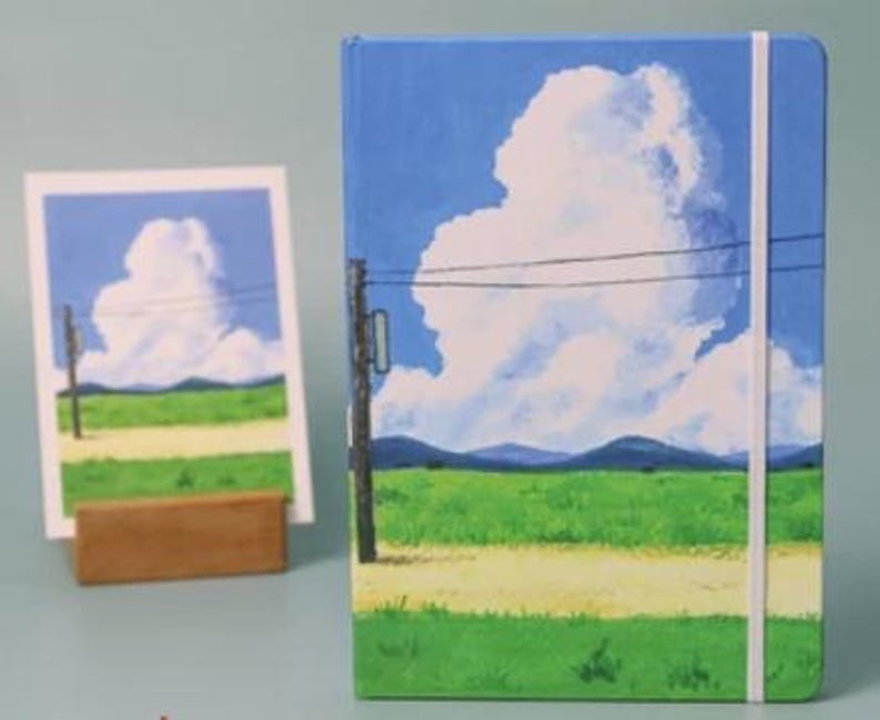 May include: A blue and green landscape notebook with a white cloud and power lines. The notebook has a white elastic band closure.
