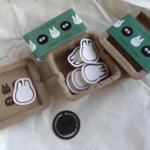 May include: A set of 14 paper clips featuring two designs: a white Totoro and a black Totoro. The clips are packaged in a brown cardboard box with a green and white label that reads "P-Clips 2 Designs 14 Pieces".