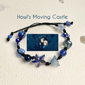 Puede incluir: Un brazalete de cuerda negra con cuentas de vidrio azul y transparente, un dije de estrella azul y blanco, y un dije con una escena de la pel&iacute;cula animada "El castillo ambulante".