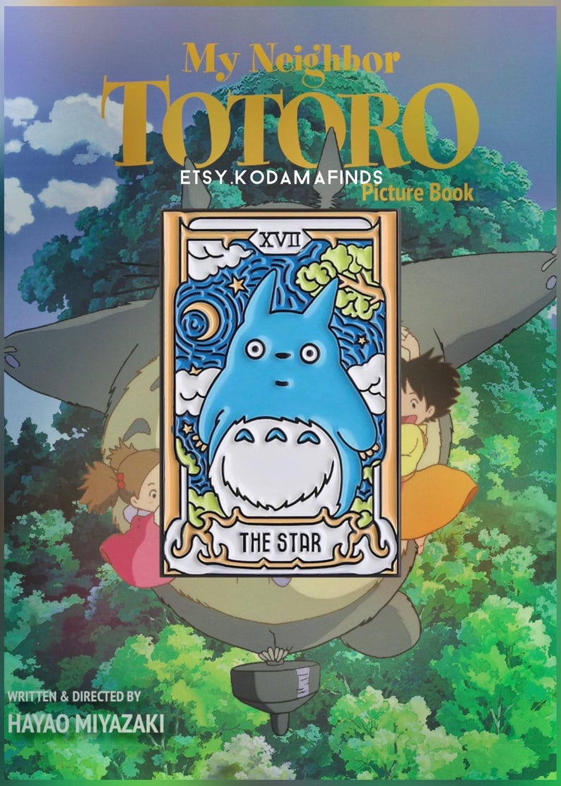 May include: A blue and white enamel pin featuring Totoro from the movie My Neighbor Totoro. The pin is in the style of a tarot card, with the number XVII and the words "The Star" on it. The pin is surrounded by a gold frame.