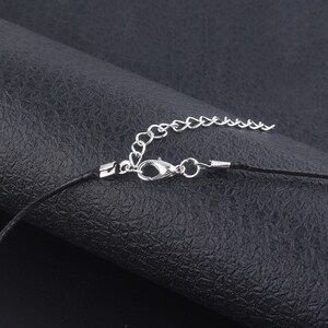 May include: Close-up of a silver chain and clasp attached to a black cord necklace.