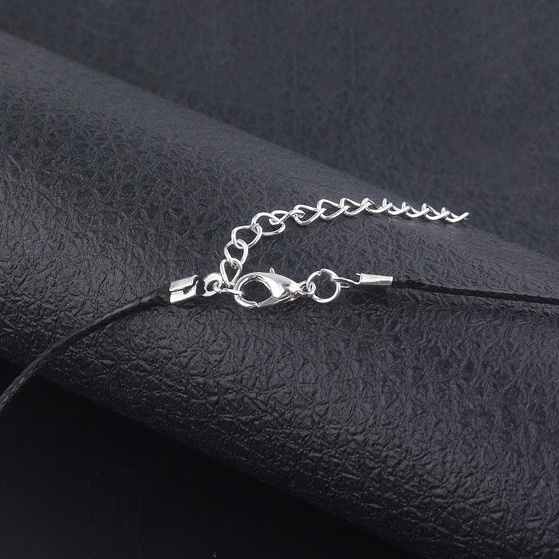 May include: Close-up of a silver chain and clasp attached to a black cord necklace.