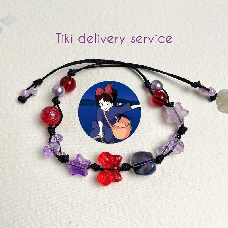 Puede incluir: Un brazalete de cuerda negra con cuentas rojas, moradas y transparentes, incluyendo un dije de estrella y un dije de mariposa. El brazalete tambi&eacute;n presenta un dije redondo con una imagen de dibujos animados de una ni&ntilde;a con un lazo rojo en el pelo.