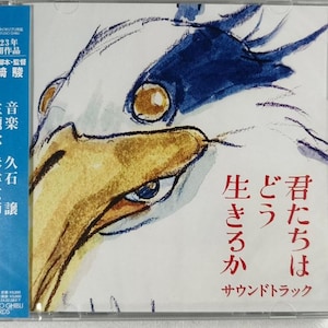 May include: A CD case with a white and blue illustration of a bird's head. The text on the case reads "2023年 公開作品 原作・脚本・監督 宮崎駿 主題歌 米津玄師 音楽 久石譲 生きろか どう 君たちは サウンドトラック".