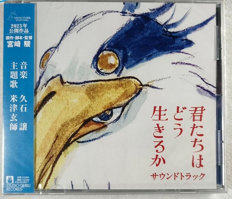 May include: A CD case with a white and blue illustration of a bird's head. The text on the case reads "2023年 公開作品 原作・脚本・監督 宮崎駿 主題歌 米津玄師 音楽 久石譲 生きろか どう 君たちは サウンドトラック".