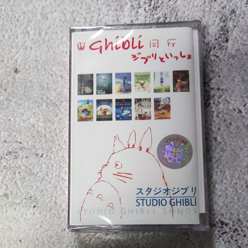 Pu&ograve; includere: Una custodia per cassette bianca con un'illustrazione rossa e nera di Totoro dal film Il mio vicino Totoro. La custodia ha il testo "與Ghioli同行 ジブリといっしょ" e "スタジオジブリ STUDIO GHIBLI STUDIO GHIBLL SONGS" stampato su di essa.