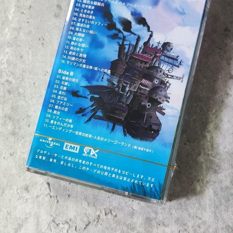 Pu&ograve; includere: Una custodia per cassette con sfondo blu e un'immagine di una casa volante. La custodia &egrave; per la colonna sonora del film "Il castello errante di Howl". Il testo sulla custodia recita "Il castello errante di Howl - Un giro di giostra della vita".