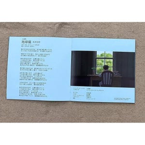 May include: A blue book with Japanese text on the left page and a black and white illustration of a person sitting at a desk looking out a window on the right page. The text on the left page includes the title "地球儀" which translates to "Globe".