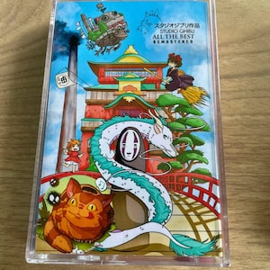 Pu&ograve; includere: Una custodia in plastica trasparente con un'illustrazione colorata di personaggi e scene di film di Studio Ghibli. Il testo sulla custodia recita "Studio Ghibli All The Best Remastered".