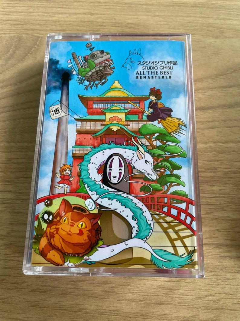 Pu&ograve; includere: Una custodia in plastica trasparente con un'illustrazione colorata di personaggi e scene di film di Studio Ghibli. Il testo sulla custodia recita "Studio Ghibli All The Best Remastered".