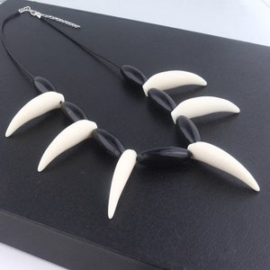 May include: Black and white necklace with a series of white fang-shaped beads and black oval beads.