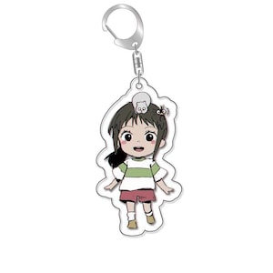 以下が含まれることがあります： 透明なアクリル製のキーホルダーで、茶色の髪の女の子の漫画のイラストが描かれています。女の子は白と緑のストライプのシャツと赤いショートパンツを着ています。彼女は小さな白い猫を抱いており、黒い鳥が彼女の頭に止まっている。