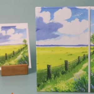 May include: A landscape notebook with a white cover and a blue sky with white clouds. The cover features a painting of a green field with a wooden fence and a path leading to a distant horizon.