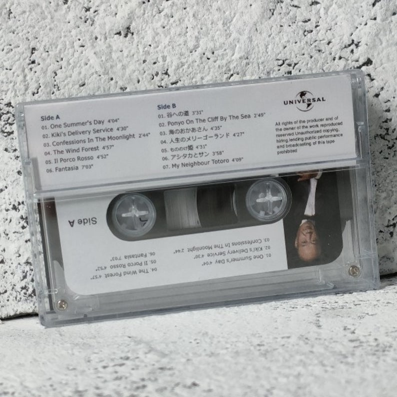 Pu&ograve; includere: Una custodia per cassette audio in plastica trasparente con un'etichetta bianca. L'etichetta riporta il titolo "Il mio vicino Totoro" e la lista delle tracce per entrambi i lati della cassetta. La custodia &egrave; etichettata "Universal" e contiene un avviso contro la copia non autorizzata.