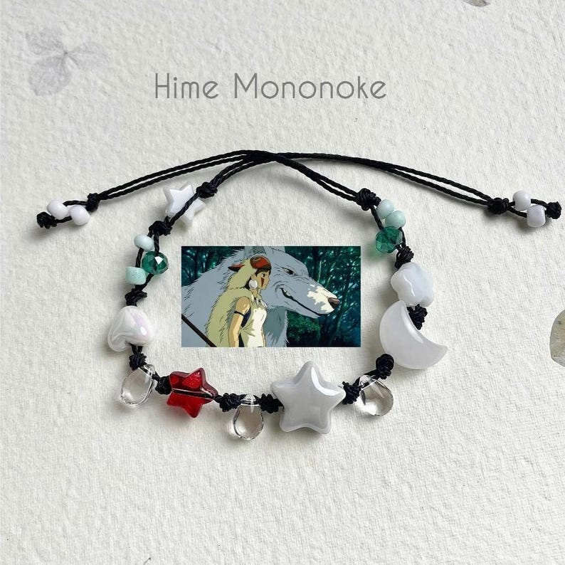 Puede incluir: Un brazalete de cuerda negra con cuentas blancas, verdes y rojas. El brazalete presenta un dije de un lobo blanco y una ni&ntilde;a de la pel&iacute;cula de anime Princesa Mononoke. El brazalete tambi&eacute;n tiene un dije con el texto "Hime Mononoke".