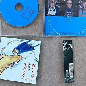 May include: A blue CD case with a white and blue bird illustration on the front. The text on the front reads "曾たちは どう 生きるか サウンドトラック".
